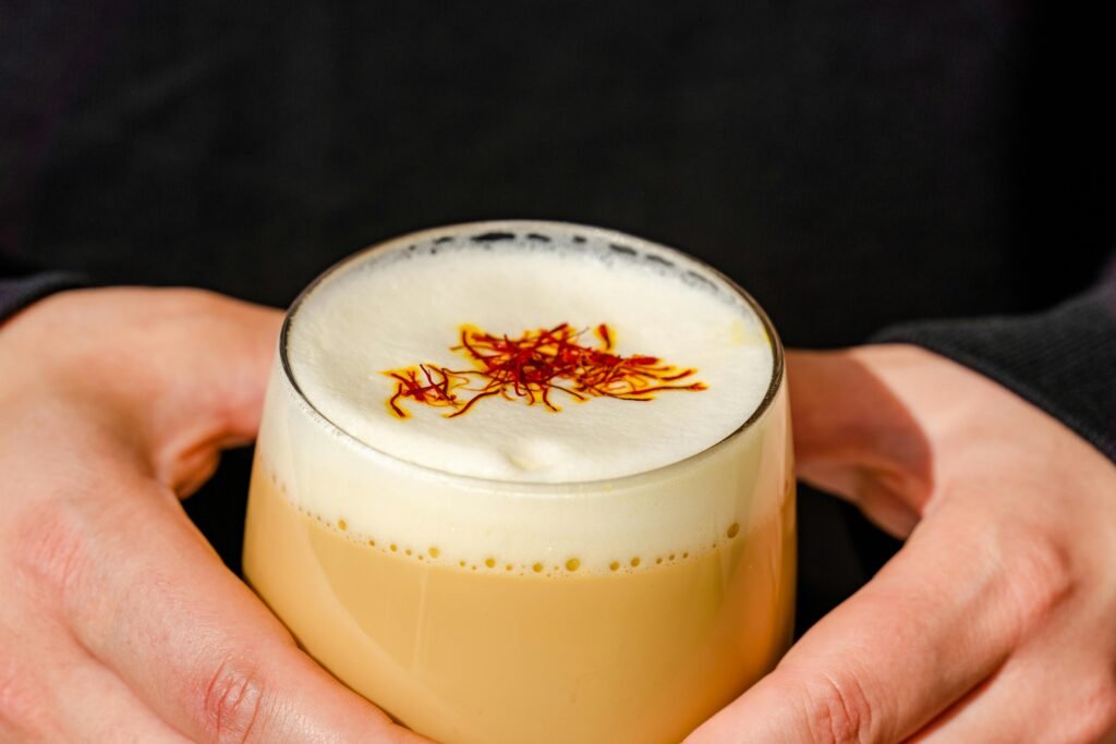 A creamy saffron milk tea held in hands, showcasing rich flavors and vibrant saffron strands.